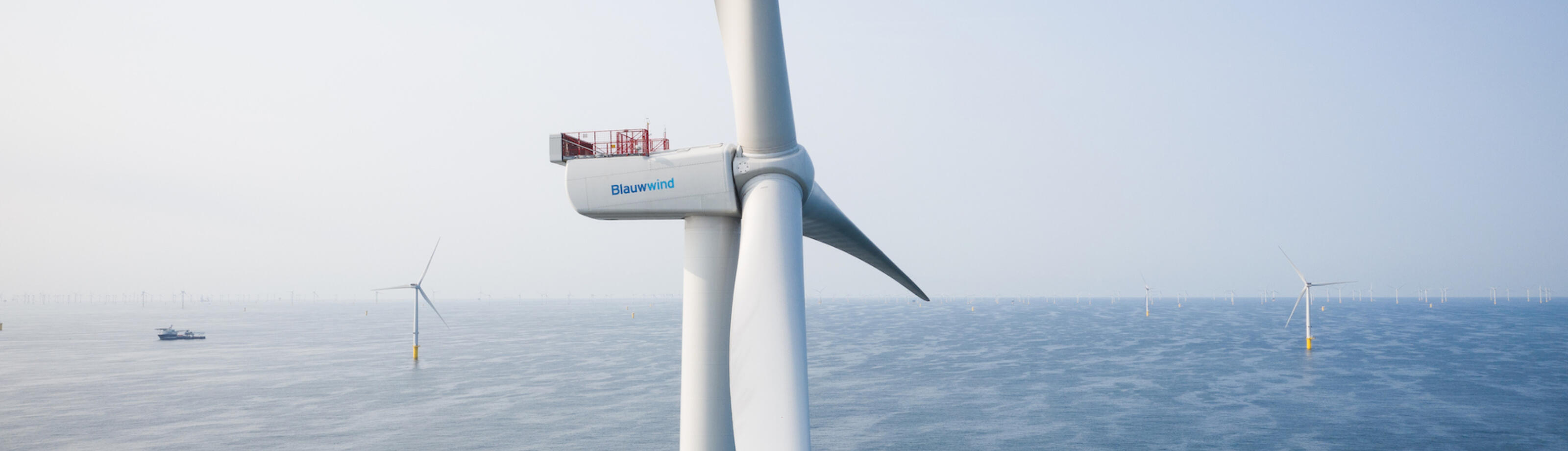A Borssele III & IV wind turbine close up with the Blauwwind logo visible and the wind farm in the background